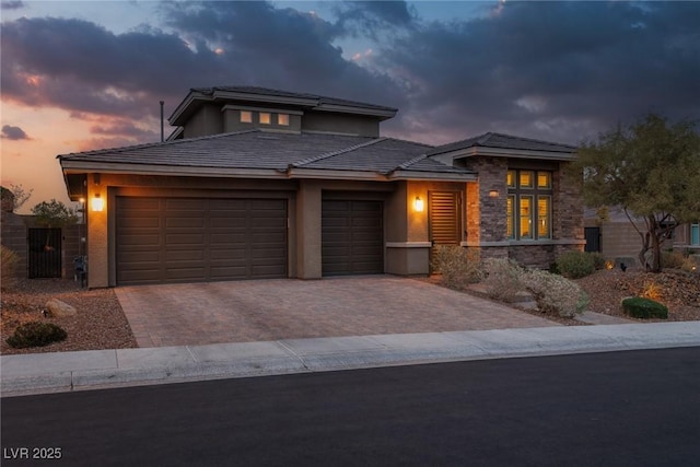 prairie-style house featuring an attached garage, stone siding, decorative driveway, and stucco siding