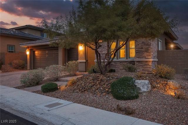 view of front of home with decorative driveway, stucco siding, an attached garage, fence, and stone siding