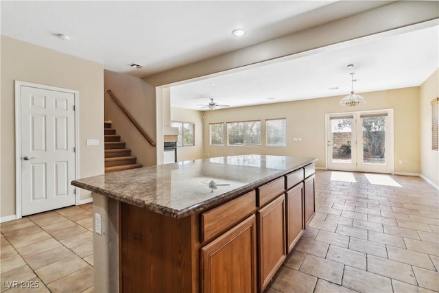 kitchen with a center island, light tile patterned floors, dark stone countertops, hanging light fixtures, and a ceiling fan