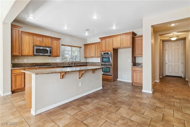 kitchen featuring a kitchen bar, brown cabinets, a sink, a center island, and appliances with stainless steel finishes