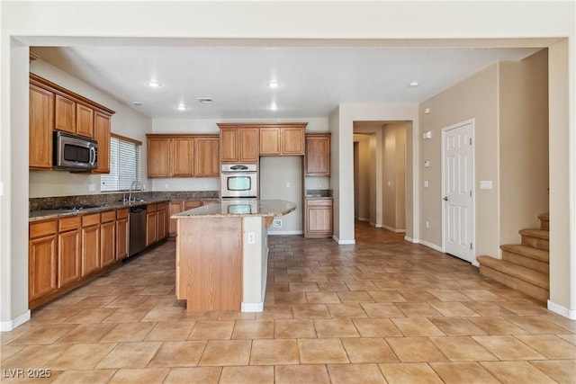 kitchen with brown cabinetry, baseboards, stone counters, stainless steel appliances, and a center island