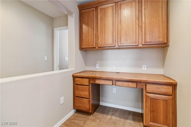 unfurnished office featuring light carpet, built in desk, and baseboards