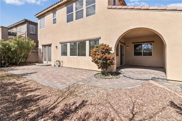 back of house with stucco siding, a tiled roof, and a patio