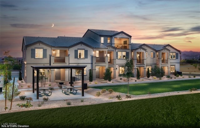 back of property with a balcony, a yard, stucco siding, and a patio