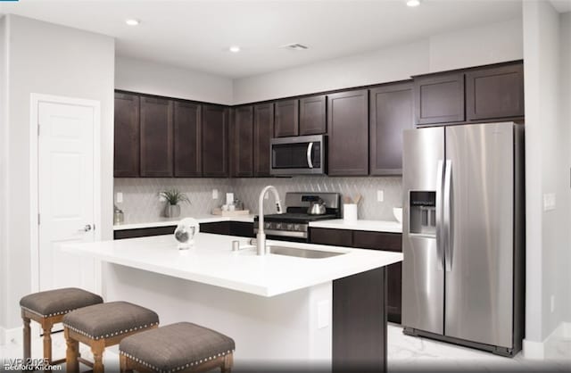 kitchen featuring dark brown cabinetry, tasteful backsplash, stainless steel appliances, light countertops, and a sink