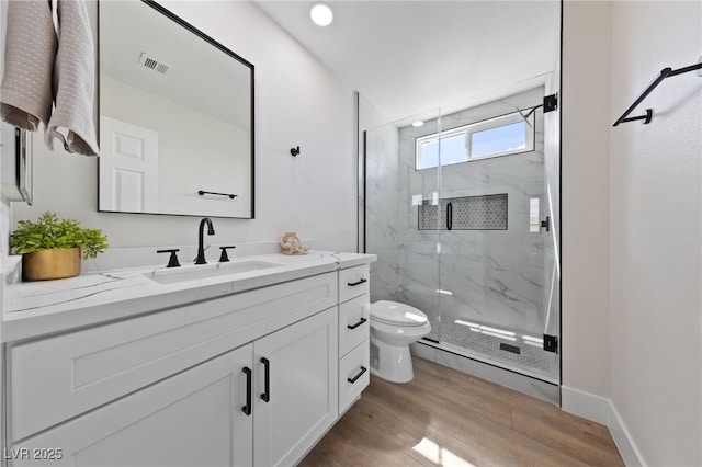 full bath featuring a marble finish shower, visible vents, toilet, vanity, and wood finished floors