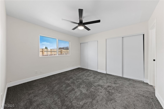 unfurnished bedroom featuring dark colored carpet, ceiling fan, baseboards, and two closets