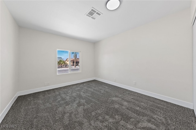 spare room with dark colored carpet, visible vents, and baseboards