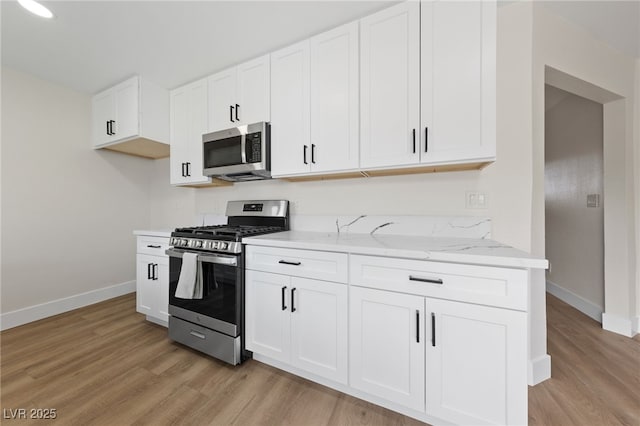 kitchen featuring light wood finished floors, baseboards, appliances with stainless steel finishes, and light stone counters