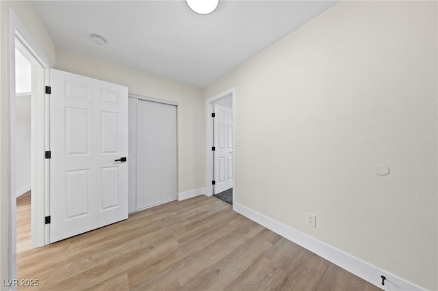 unfurnished bedroom with light wood-type flooring, baseboards, and a closet