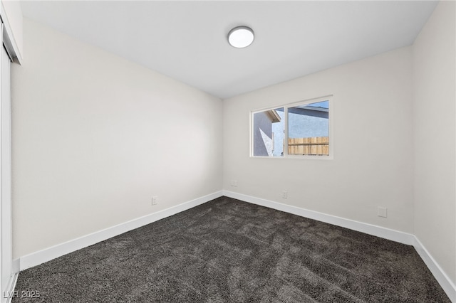 spare room featuring dark carpet and baseboards