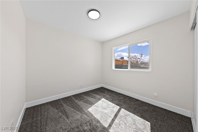 spare room featuring dark colored carpet and baseboards