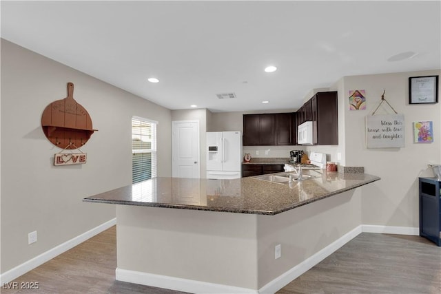 kitchen featuring white appliances, a sink, visible vents, dark brown cabinets, and dark stone counters