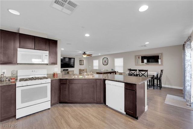 kitchen featuring dark brown cabinetry, white appliances, visible vents, and light wood-style floors