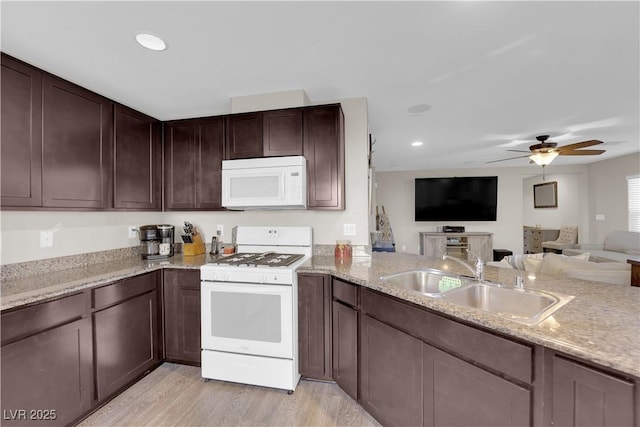 kitchen with dark brown cabinetry, white appliances, a sink, open floor plan, and light wood-type flooring