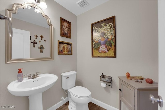 half bathroom with toilet, baseboards, visible vents, and a sink