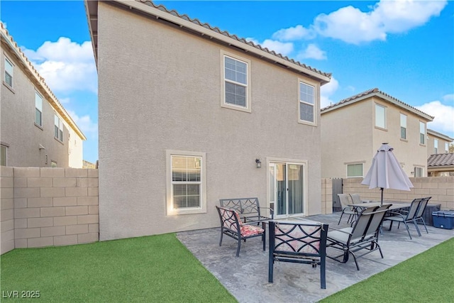 rear view of property with stucco siding, a lawn, a patio area, a fenced backyard, and a tiled roof