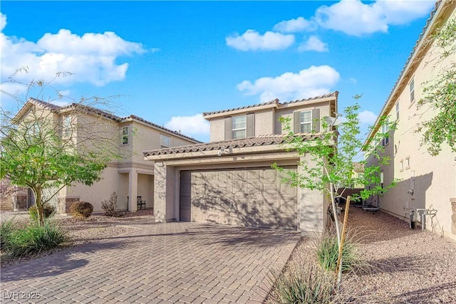 mediterranean / spanish-style home with decorative driveway, an attached garage, a tile roof, and stucco siding