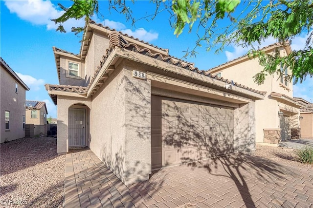 view of home's exterior with decorative driveway, stucco siding, an attached garage, fence, and a tiled roof