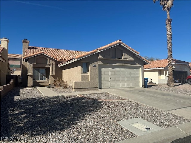 mediterranean / spanish home featuring an attached garage, a tile roof, driveway, stucco siding, and a chimney