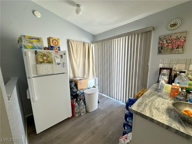 kitchen with a sink, vaulted ceiling, wood finished floors, and freestanding refrigerator