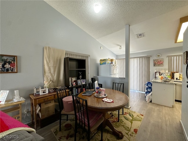 dining area with lofted ceiling, a textured ceiling, wood finished floors, and visible vents