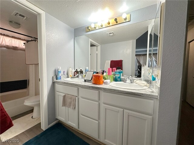 bathroom featuring a textured ceiling, double vanity, a sink, and toilet