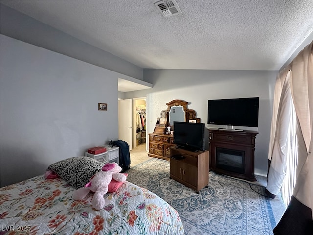 bedroom with a textured ceiling, visible vents, vaulted ceiling, a spacious closet, and carpet