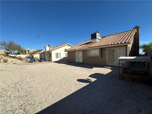 rear view of house with central air condition unit, a chimney, a tile roof, and stucco siding