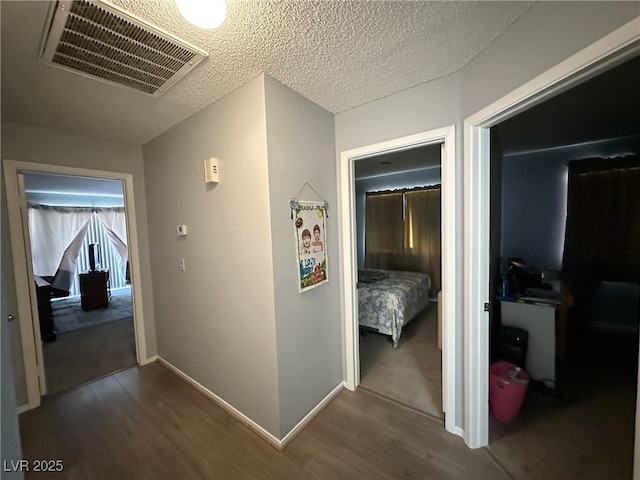 hall with visible vents, dark wood finished floors, a textured ceiling, and baseboards