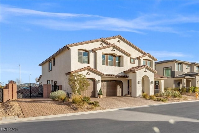 mediterranean / spanish house featuring a garage, a gate, a tiled roof, and stucco siding