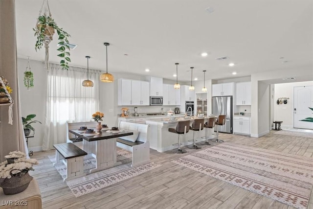 kitchen with white cabinetry, a center island with sink, appliances with stainless steel finishes, and a breakfast bar area