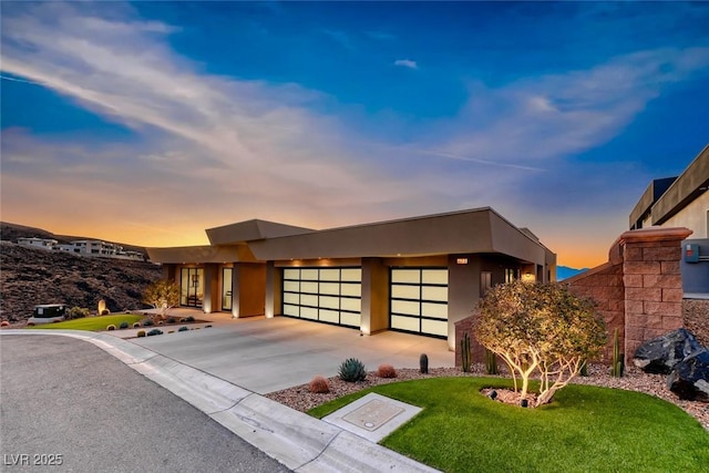 contemporary home featuring a yard, driveway, an attached garage, and stucco siding