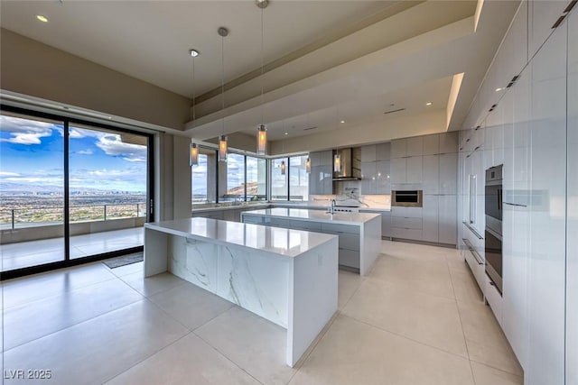 kitchen featuring pendant lighting, a spacious island, gray cabinetry, wall chimney range hood, and modern cabinets