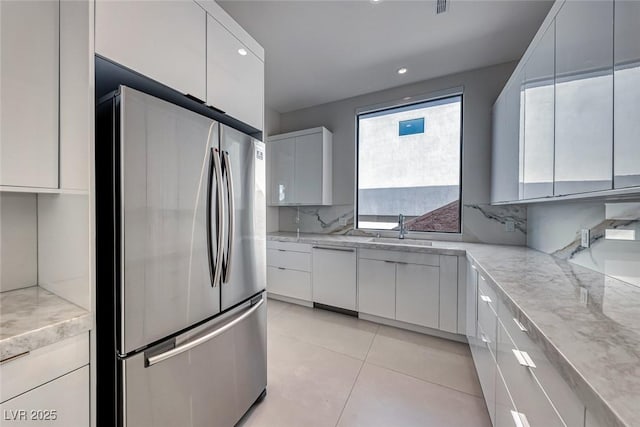 kitchen with white dishwasher, a sink, white cabinets, freestanding refrigerator, and decorative backsplash