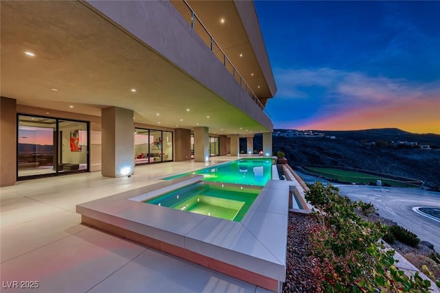 pool at dusk with a patio and an in ground hot tub