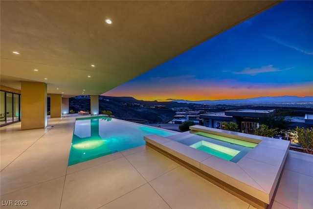 view of pool with an infinity pool, an in ground hot tub, a patio, and a mountain view