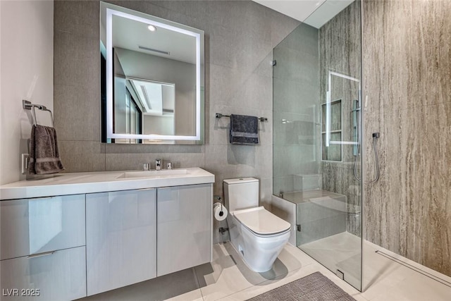 bathroom featuring tile walls, toilet, a tile shower, vanity, and tile patterned floors