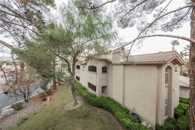 view of side of home with stucco siding, a tile roof, and a yard