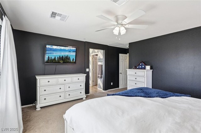 bedroom with a ceiling fan, light colored carpet, visible vents, and ensuite bathroom