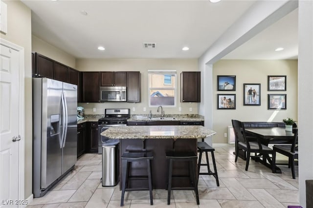 kitchen featuring visible vents, light stone counters, appliances with stainless steel finishes, a breakfast bar, and a sink