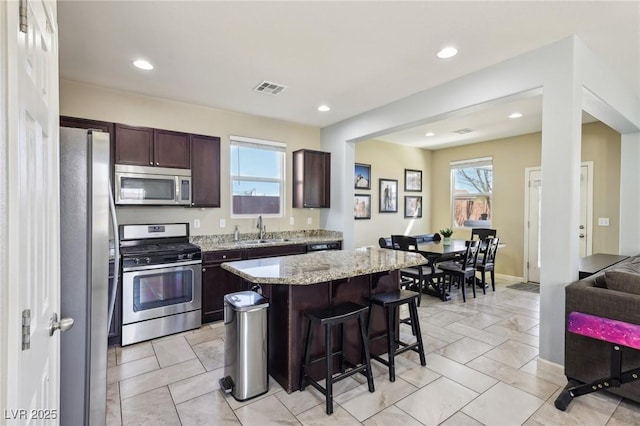 kitchen with a center island, a breakfast bar area, appliances with stainless steel finishes, dark brown cabinetry, and a sink