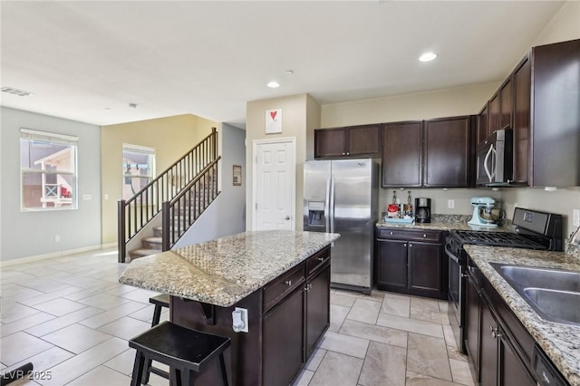 kitchen with light stone counters, a breakfast bar, appliances with stainless steel finishes, dark brown cabinetry, and a kitchen island