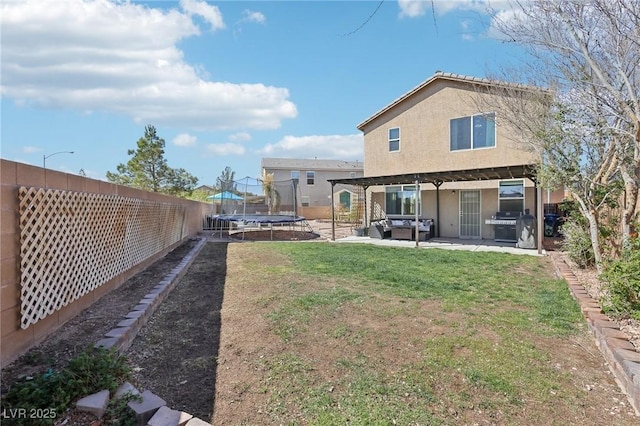 rear view of property with a lawn, a fenced backyard, a trampoline, a patio area, and stucco siding