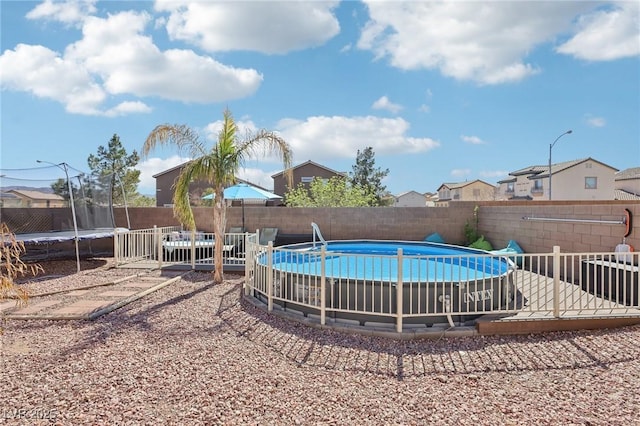 view of swimming pool with a trampoline, a residential view, a fenced backyard, and a fenced in pool