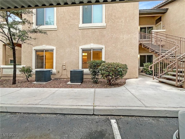 exterior space with stucco siding, central air condition unit, and stairway