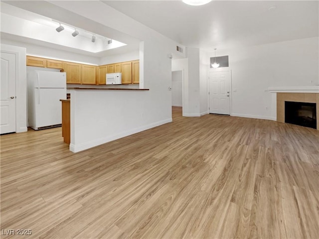 unfurnished living room featuring a tiled fireplace, visible vents, light wood-style flooring, and baseboards