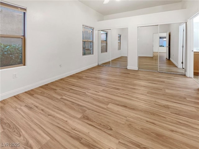 unfurnished bedroom featuring multiple windows, baseboards, light wood-type flooring, and two closets