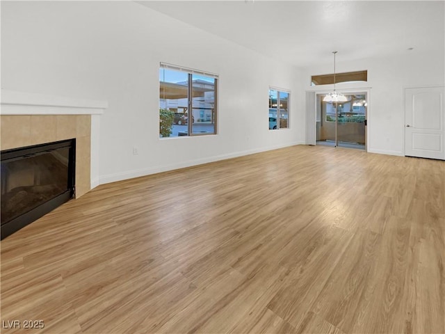 unfurnished living room featuring a notable chandelier, a fireplace, baseboards, and light wood finished floors