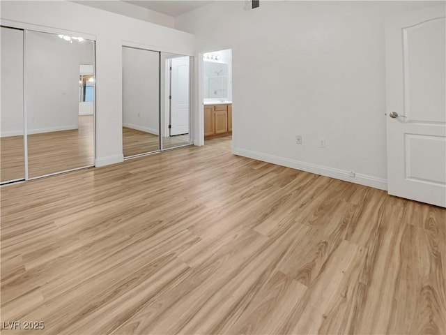 unfurnished bedroom with baseboards, two closets, and light wood finished floors